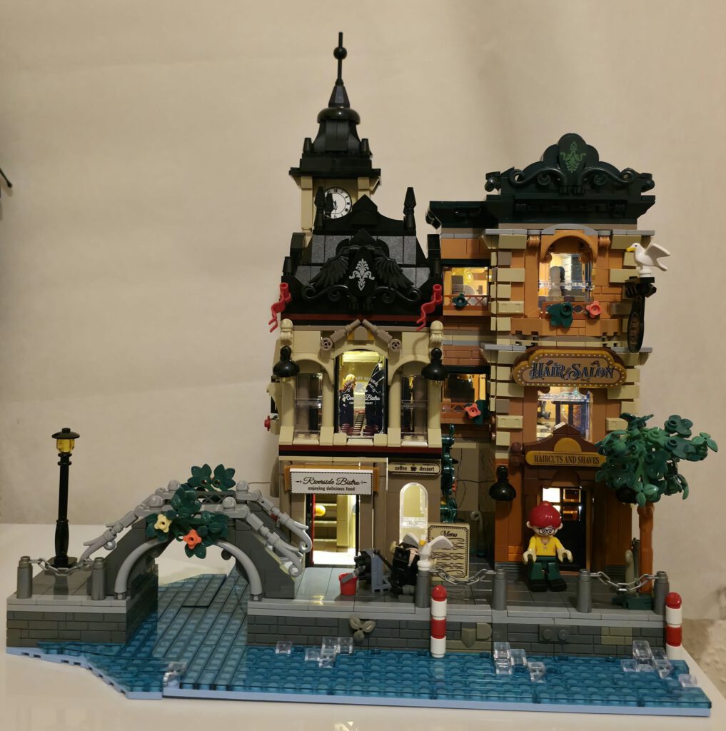 Komplett aufgebautes IAMBRICK Riverside Bistro & Hair Salon mit zwei Gebäuden, Uhrenturm, Brücke und Wasserlandschaft.