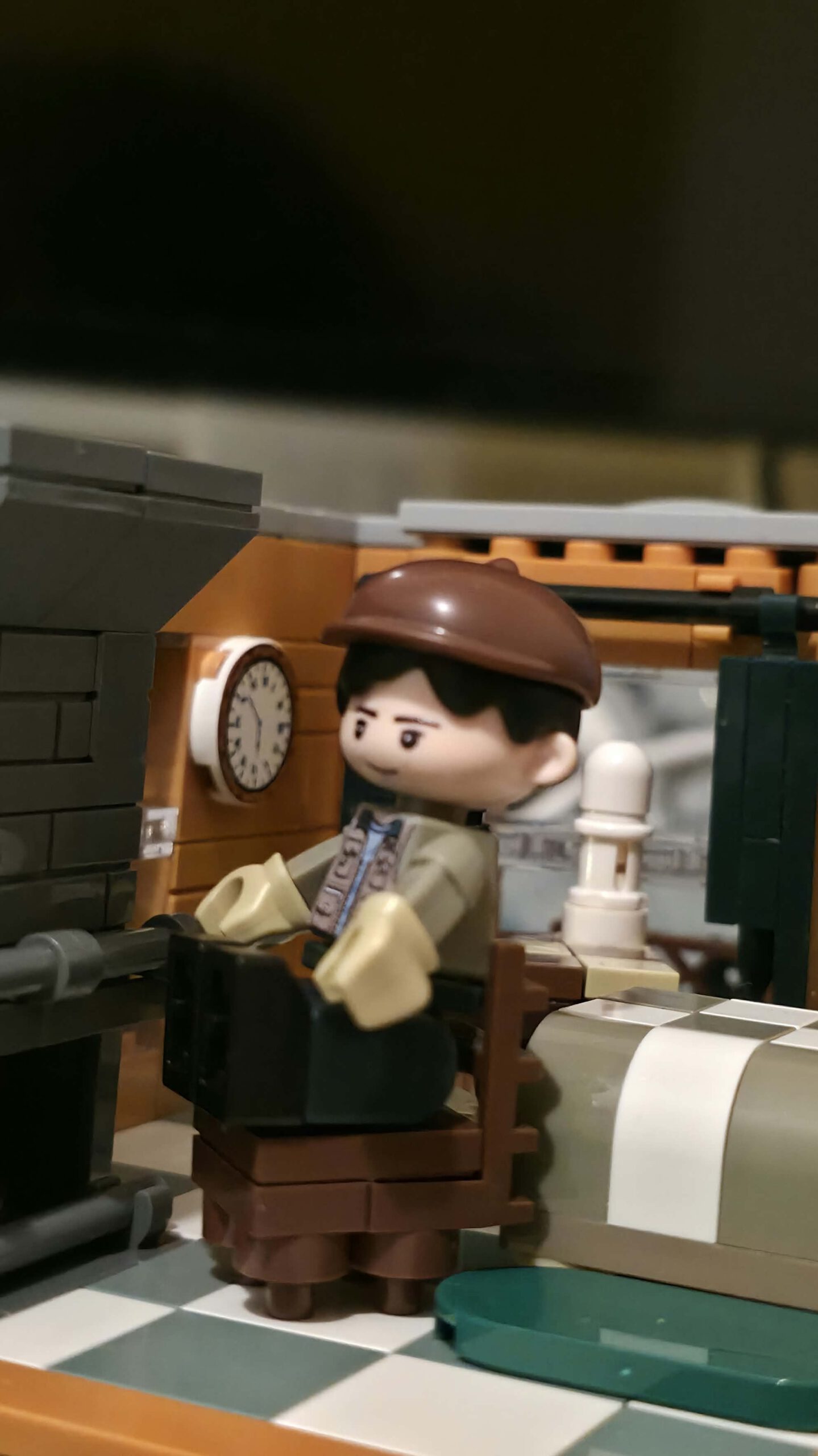 IAMBRICK Figur mit brauner Kappe in einem eingerichteten Wohnraum mit Wanduhr und Möbeln